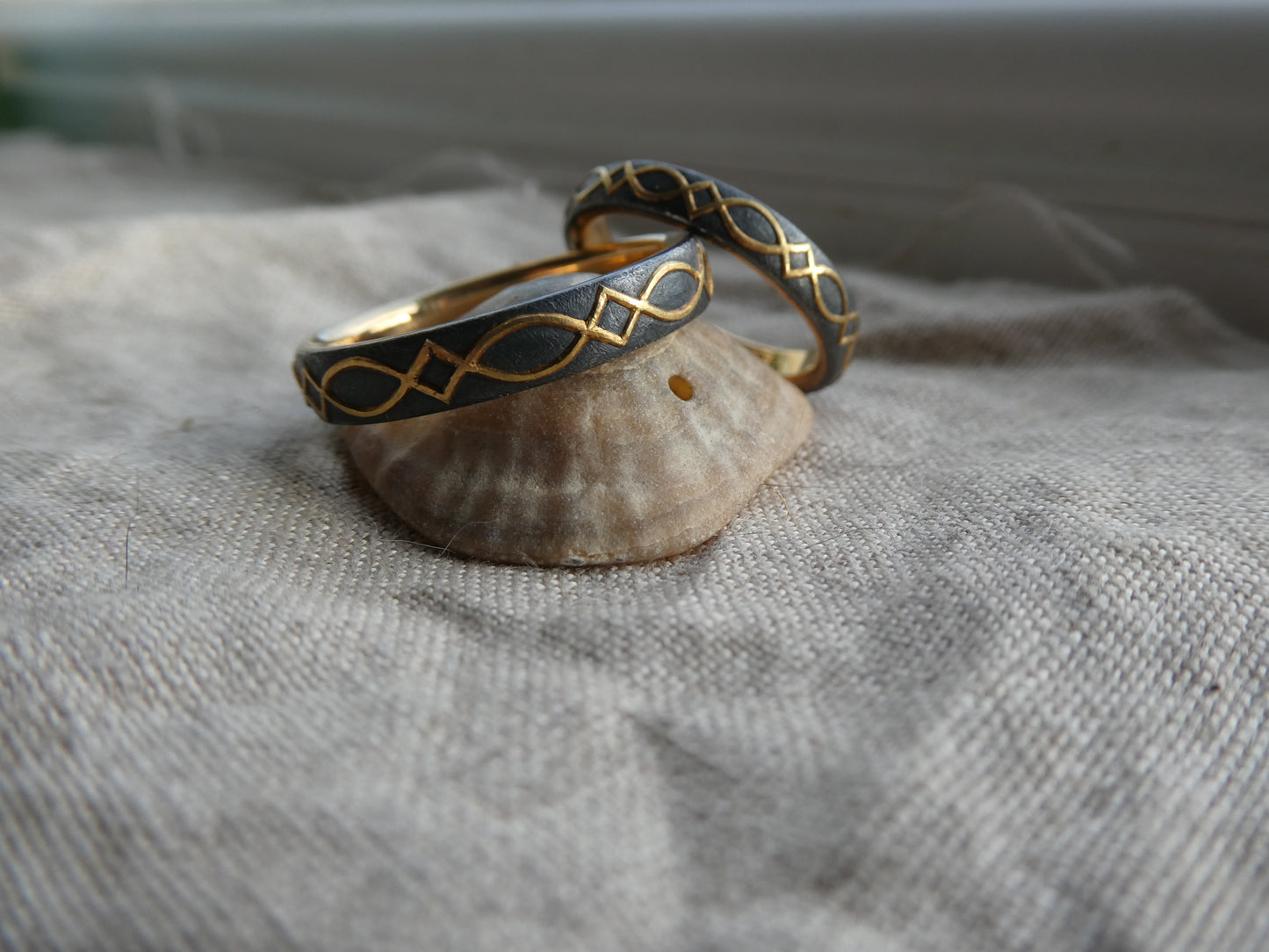 gold inlaid wedding bands with design set against blackened silver, displayed on shell
