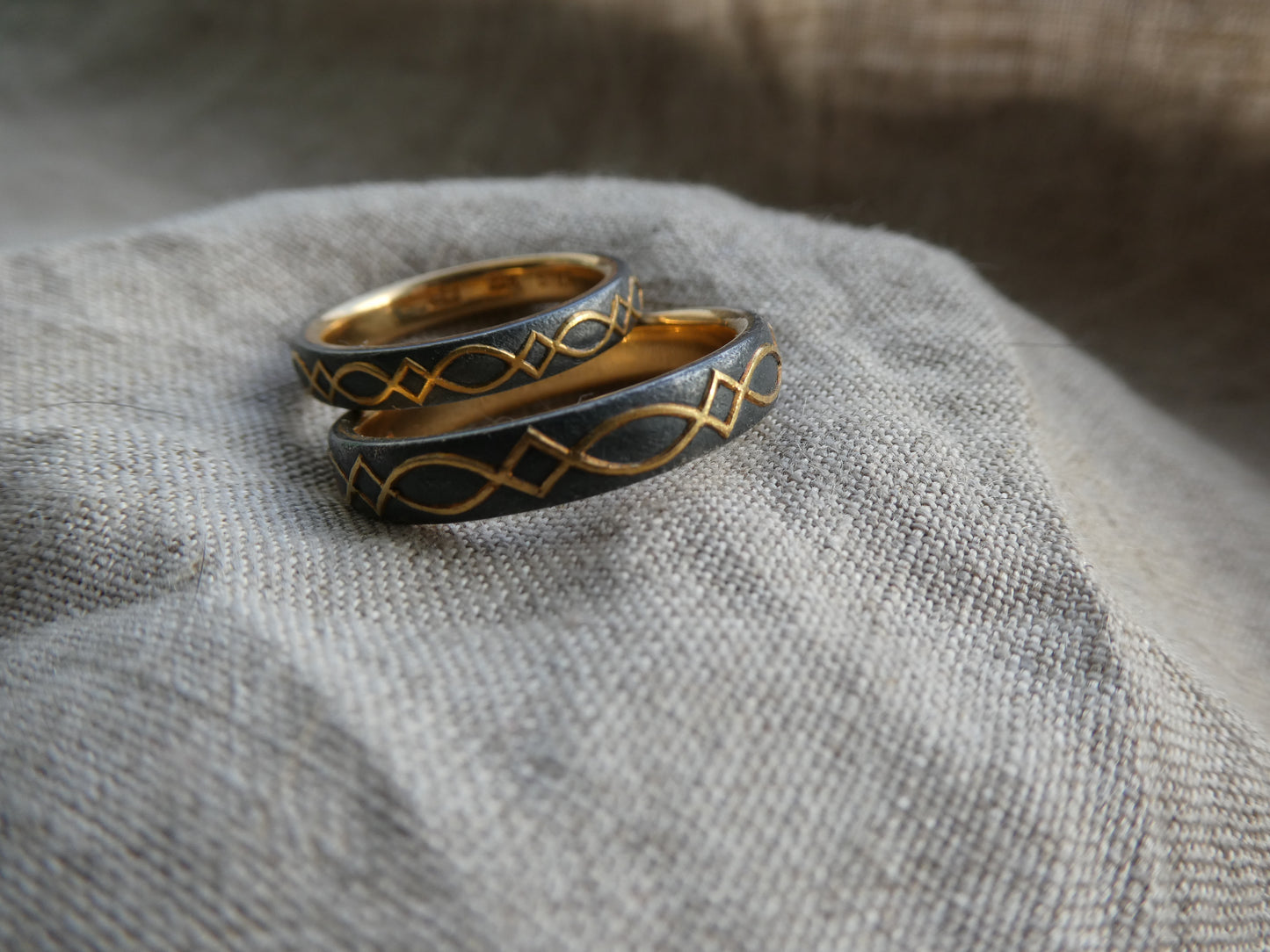 gold inlaid wedding bands with design set against blackened silver, pictured on linen