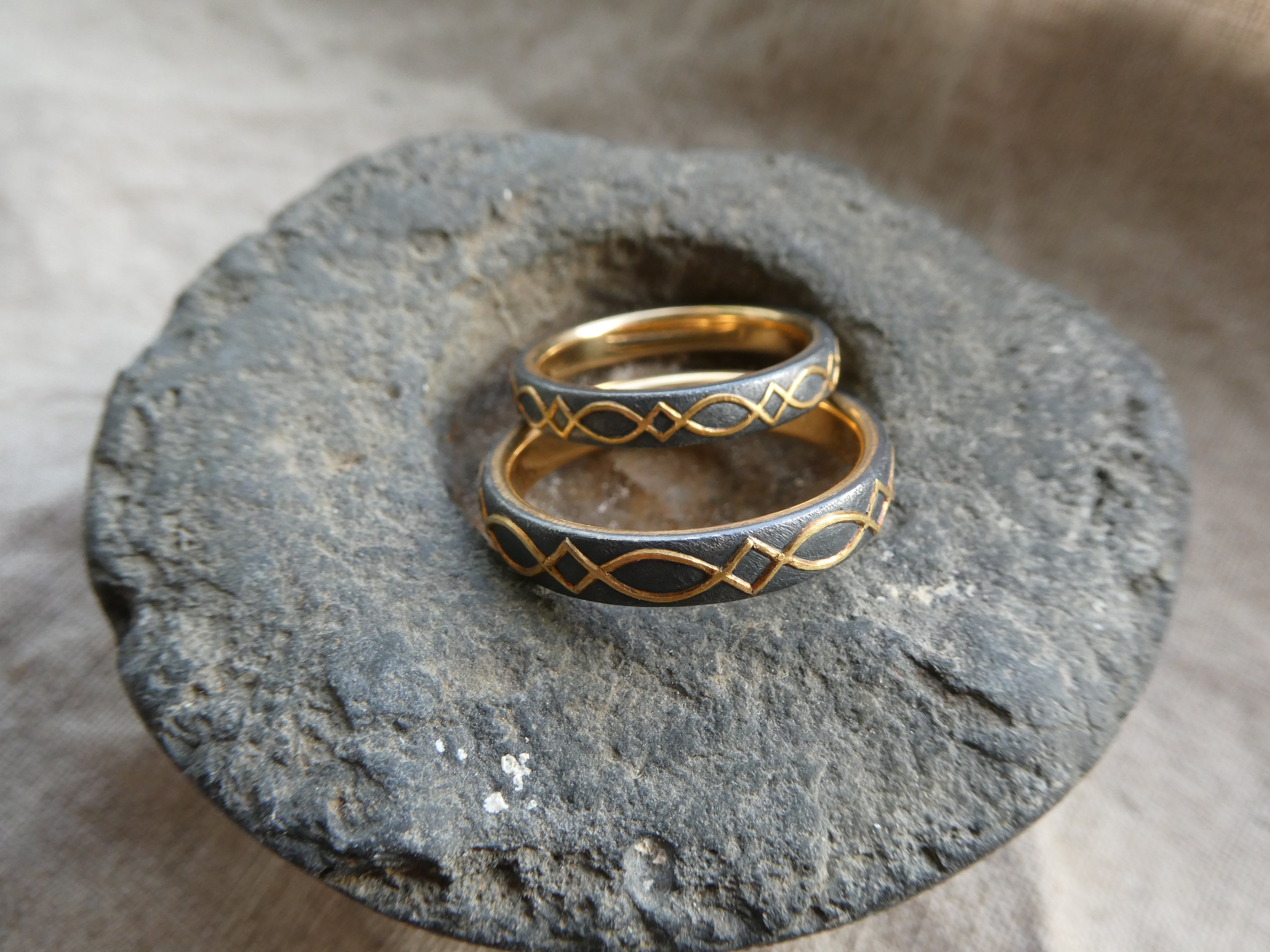gold inlaid wedding bands with design set against blackened silver. pictured on stone.
